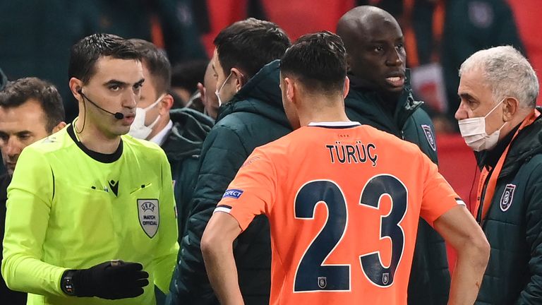 Romanian referee Ovidiu Hategan (L) talks to Istanbul Basaksehir FK staff members and forward Demba Ba 