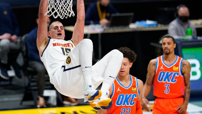 Denver Nuggets center Nikola Jokic, left, hangs from the rim after dunking the ball for a basket against Oklahoma City Thunder forward Isaiah Roby, center, and guard George Hill in the first half of an NBA basketball game Tuesday, Jan. 19, 2021, in Denver.