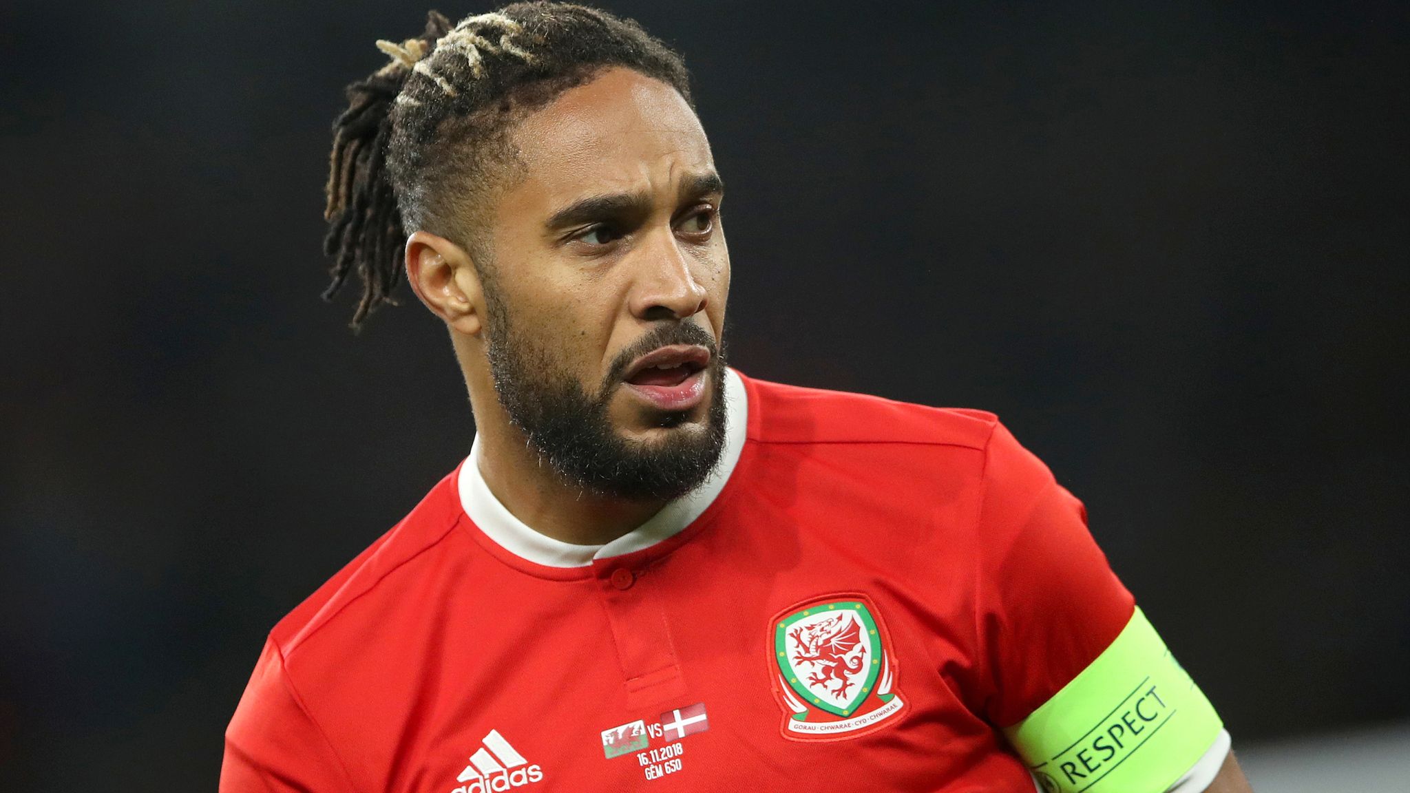  Ashley Williams, a soccer player wearing a red jersey with the number 6 on it, has fallen to the ground during a match and is lying on his back with his eyes closed.