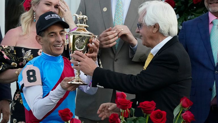 Trainer Bob Baffert hands the winner's trophy to jockey John Velazquez after they victory with Medina Spirit in the 147th running of the Kentucky Derby at Churchill Downs, Saturday, May 1, 2021, in Louisville, Ky. (AP Photo/Jeff Roberson)