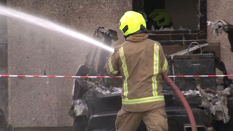 A firefighter helps extinguish the blaze in front of a burnt-out vehicle