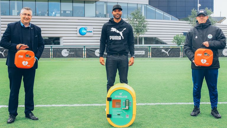 Former Manchester City player Joleon Lescott (centre) presenting one of the AED's to local team Collyhurst Youth Junior Football Club.