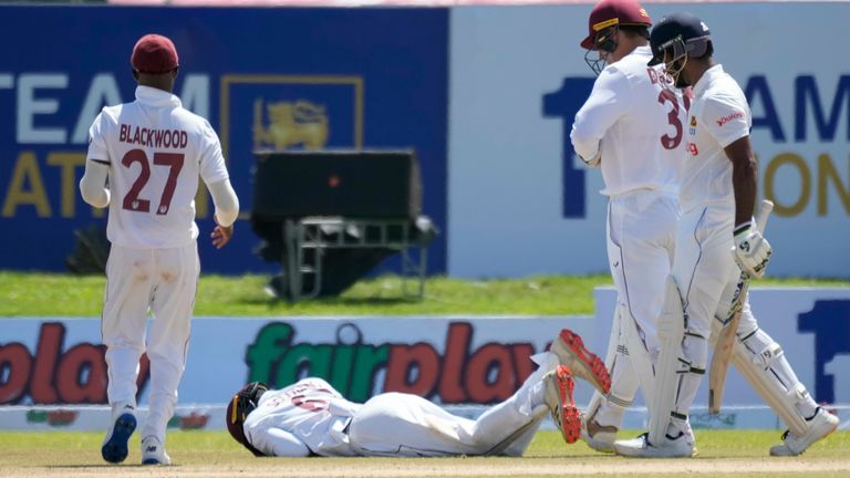 West Indies' fielder Jeremy Solozano lies on the ground after being hit by a shot played by Sri Lanka's Dimuth Karunaratne, right, during the day one of the first Test between Sri Lanka and West Indies' in Galle, Sri Lanka, Sunday, Nov. 21, 2021. (AP Photo/Eranga Jayawardena)