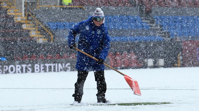 A member of the groundstaff scrapes snow from the lines as the snow falls ahead of the English Premier League football match between Burnley and Tottenham Hotspur at Turf Moor in Burnley, north west England on November 28, 2021