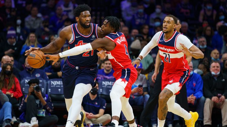 Washington Wizards' Aaron Holiday, center, knocks the ball away from Philadelphia 76ers' Joel Embiid, left, during the first half of an NBA basketball game, Wednesday, Feb. 2, 2022, in Philadelphia
