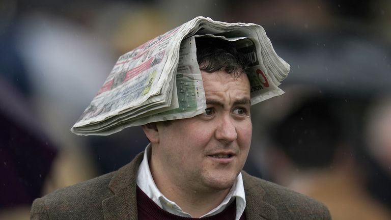 A racegoer uses a soggy newspaper to shelter from the rain at Cheltenham