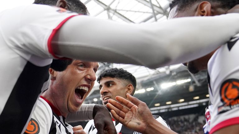 Arjan Raikhy se voltea y sonríe mientras los jugadores de Grimsby celebran