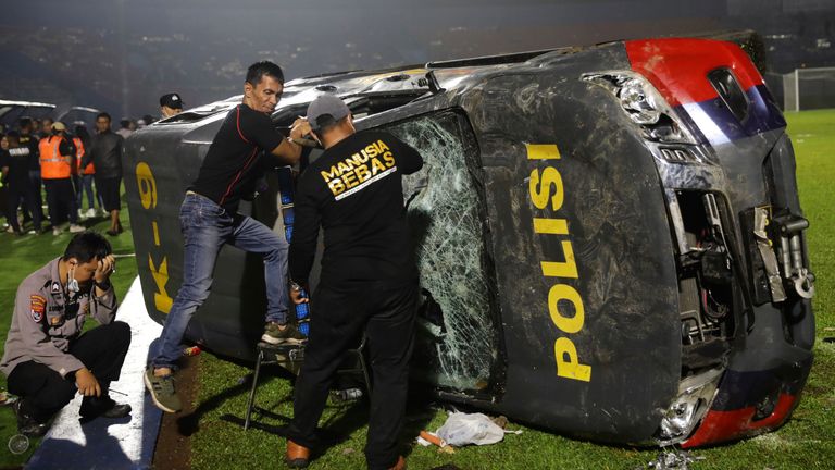 Officers examine a damaged police vehicle following a clash between supporters of two Indonesian soccer teams at Kanjuruhan Stadium in Malang, East Java, Indonesia on Saturday, Oct. 1, 2022. Panic following the Police actions left more than 100 people dead, most trampled to death, police said Sunday.  (AP Photo/Yudha Prabowo)