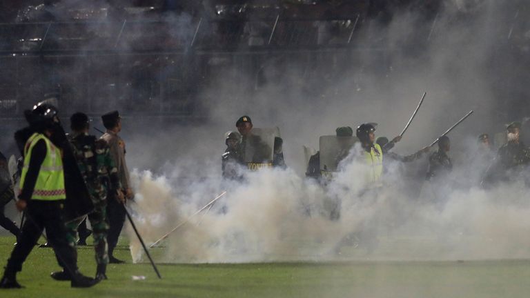 Police and soldiers stand amid tear gas smoke after clashes between fans during a football match at Kanjuruhan Stadium in Malang, East Java, Indonesia, Saturday, Oct. 1, 2022. Panic following the Police actions left more than 100 people dead, most trampled to death, police said on Sunday.  (AP Photo/Yudha Prabowo)