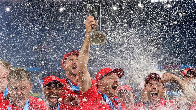 England&#39;s captain Jos Buttler, center, holds the trophy as players spray champagne while they celebrate after defeating Pakistan in the final of the T20 World Cup Cricket tournament at the Melbourne Cricket Ground in Melbourne, Australia, Sunday, Nov. 13, 2022. (AP Photo/Asanka Brendon Ratnayake)