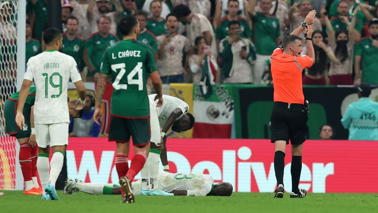 English referee Michael Oliver indicates to his wristwatch as he stops play and time for an injury to Saudi Arabia's Abdullah Madu at the World Cup in Qatar
