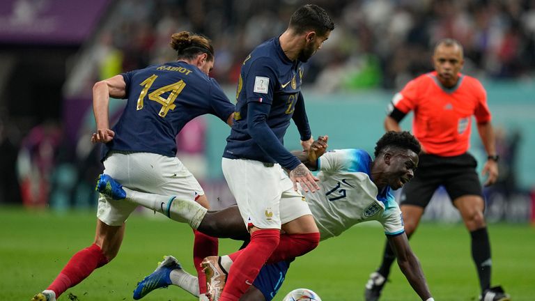 England&#39;s Bukayo Saka falls while battling for the ball with France&#39;s Theo Hernandez, center, and Adrien Rabiot during the World Cup quarterfinal soccer match between England and France, at the Al Bayt Stadium in Al Khor, Qatar, Saturday, Dec. 10, 2022. (AP Photo/Abbie Parr)