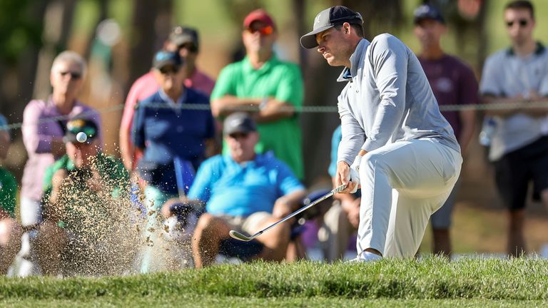 Adam Schenk punches out of the bunker (AP Photo/Mike Carlson)