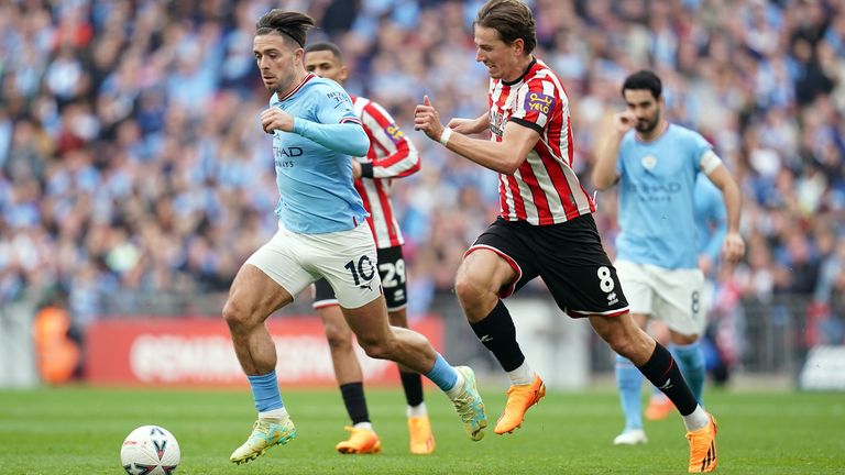 Jack Grealish runs with the ball under pressure from Sander Berge