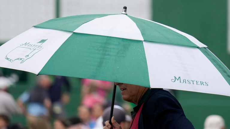 A spectator walks in the rain past the main leaderboard during the first round at the Masters golf tournament on Thursday, April 7, 2022, in Augusta, Ga. (AP Photo/Matt Slocum)