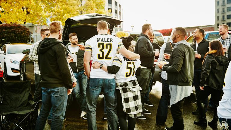 Couple wearing football jerseys embracing during tailgating party in stadium parking lot