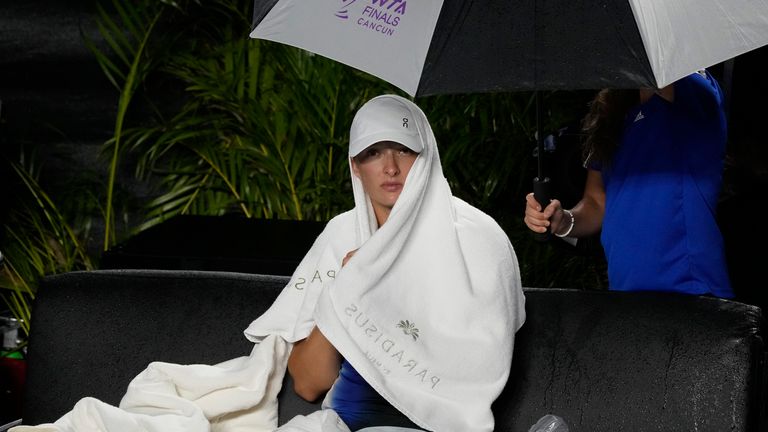 Iga Swiatek, of Poland, uses a towel as protection from the rain during a pause in the women&#39;s singles semifinal match against Aryna Sabalenka, of Belarus, at the WTA Finals tennis championships, in Cancun , Mexico, Saturday, Nov. 4, 2023. (AP Photo/Fernando Llano)
