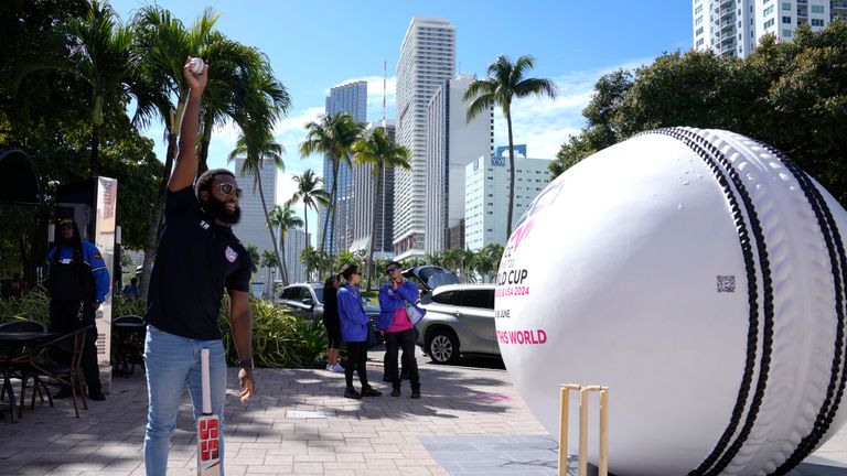 Aaron Jones, vice-captain of Team USA, demonstrates a bowling technique as he stands next to a giant cricket ball at an event marking 100 days until the ICC men's T20 Cricket World Cup 2024 is held in the United States