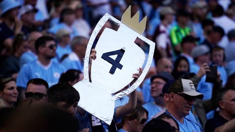 Manchester City fans raise a cardboard Premier League trophy reflecting their club's four successive title wins
