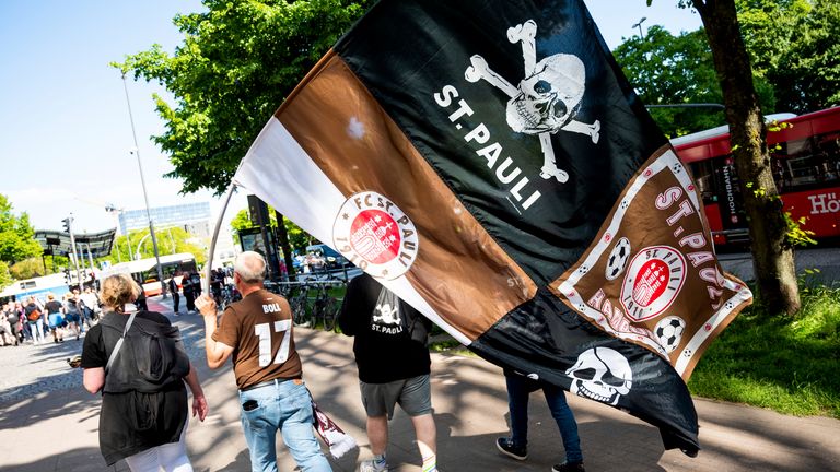 12 May 2024, Hamburg: Soccer: 2nd Bundesliga, FC St. Pauli - VfL Osnabr'ck, 33rd matchday, in front of the Millerntor Stadium. Fans walk across the Reeperbahn with a large banner. FC St. Pauli is promoted to the Bundesliga ahead of schedule. 