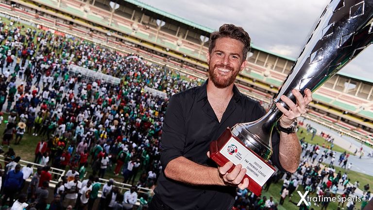 Nairobi, Kenya. 25 Jun 2023. Johnathan MCKINSTRY (Head Coach, Gor Mahia) with the 2022-23 KPL league winners trophy. In the background, Gor Mahia fans who had flooded onto to the pitch following the final whistle Nairobi City Stars v Gor Mahia, Kenyan Premier League. Gor Mahia won 4-1, becoming Champions of the Kenyan Premier League. Kasarani Stadium. Credit: XtraTimeSports (Darren McKinstry)