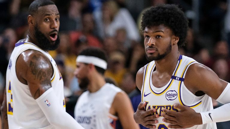 Los Angeles Lakers guard Bronny James (9), right, steps onto the court with Los Angeles Lakers forward LeBron James (23) during the first half of a preseason NBA basketball game on Sunday, Oct. 6, 2024, in Palm Desert, California. (AP Photo/William Liang)