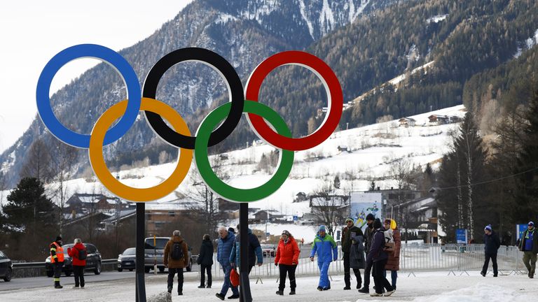 People walk near Olympic rings near the village of Anterselva where the Biathlon will take place during the Milan Cortina 2026 Winter Olympics, in northern Italy, Saturday, Jan. 25, 2025. (AP Photo/Alessandro Trovati)