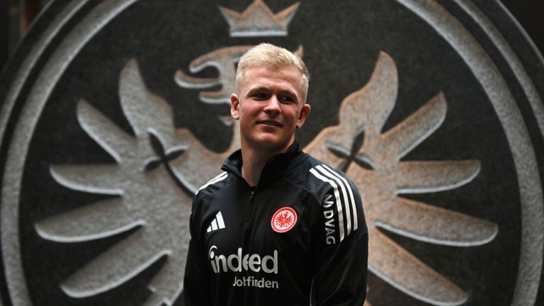 New signing Jonathan Burkardt stands in front of a stone eagle logo after the Eintracht Frankfurt press conference at the professional campu