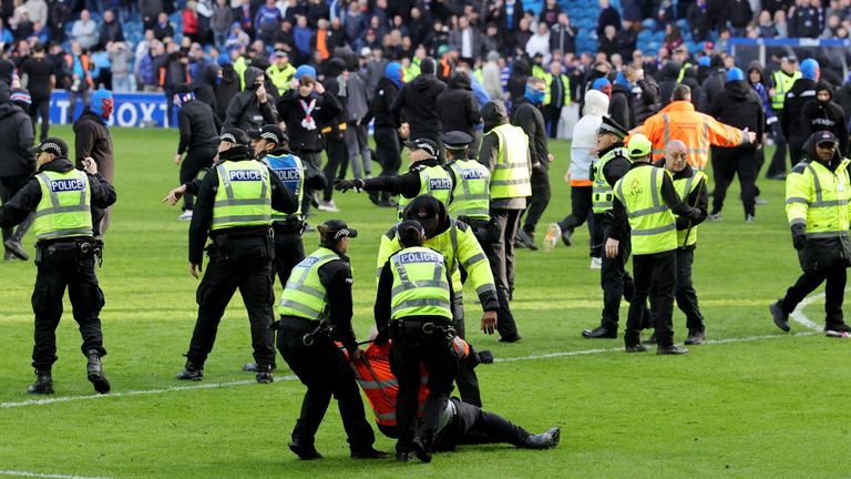 Um comissário ferido é ajudado por policiais enquanto torcedores invadem o campo em Ibrox