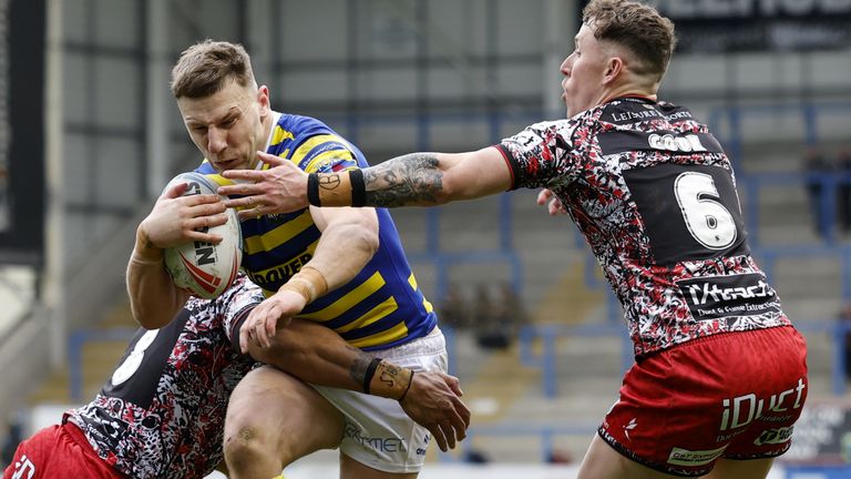 George Williams (al centro) dei Warrington Wolves viene affrontato da Joe Ofahengaue dei Leigh Leopards (a sinistra) e Adam Cook (a destra) 
