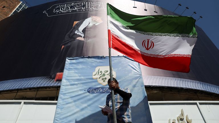 A man holds an Iranian flag on a street, after U.S. and Iranian officials said they had reached a deal to end their war and reopen the Strai