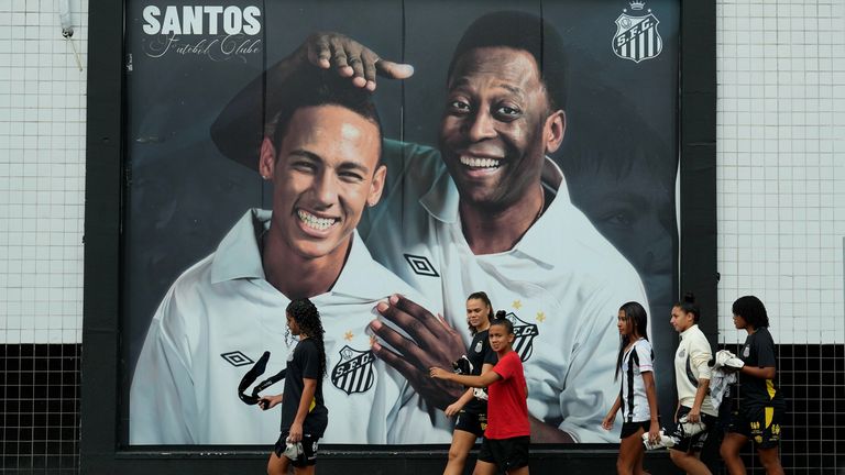 Santos fans walk past a mural of late football legend Pele, right, and Neymar outside Vila Belmiro Stadium in Santos, Brazil
