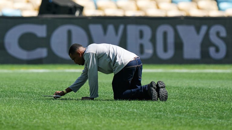 A worker cuts grass with scissors on the field ahead of the clash between the Cowboys and the Ravens