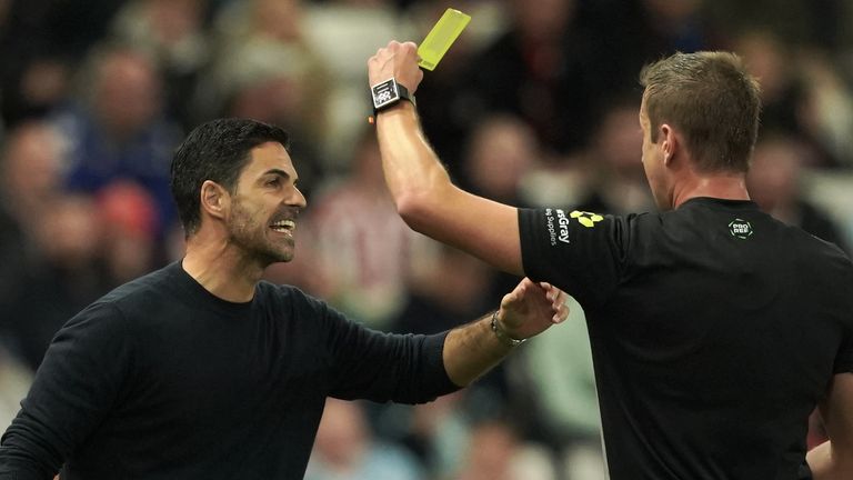 Referee John Brooks shows Mikel Arteta a yellow card in the first half