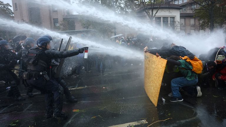 Protesters take cover behind a plywood board as riot police use a water canon in Paris. Pic: Reuters