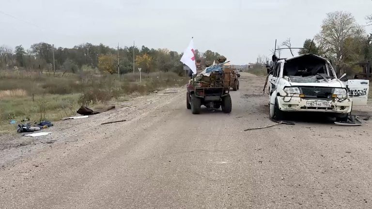 Russian military personnel pass by damaged vehicle during a demining operation conducted by them in the Russian-controlled Ukrainian town of